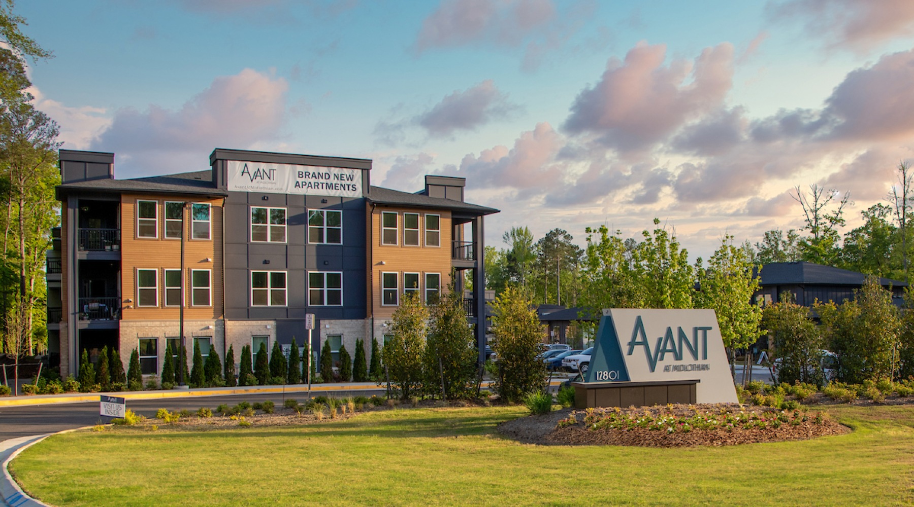 Exterior view of Avant at Midlothian, a modern apartment community featuring a three-story building with contemporary finishes, surrounded by greenery and a large monument sign at the entrance.