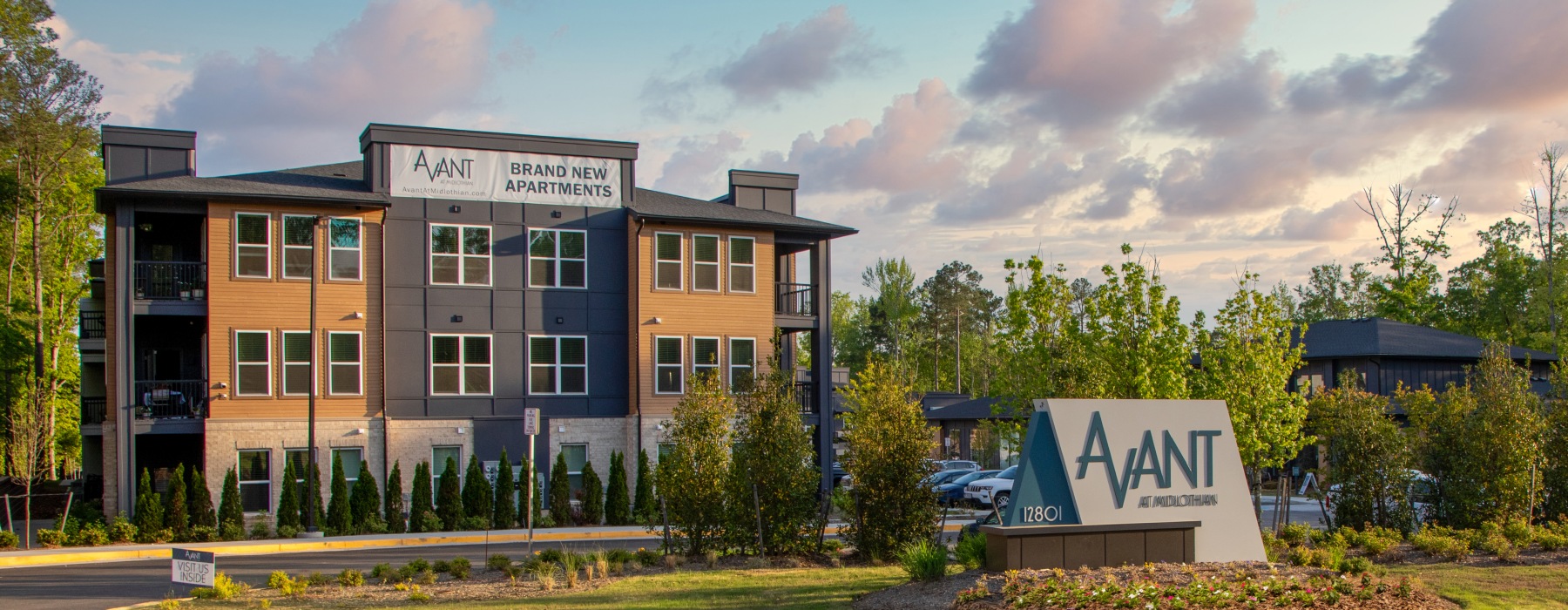 Exterior view of Avant at Midlothian, a modern apartment community featuring a three-story building with contemporary finishes, surrounded by greenery and a large monument sign at the entrance.